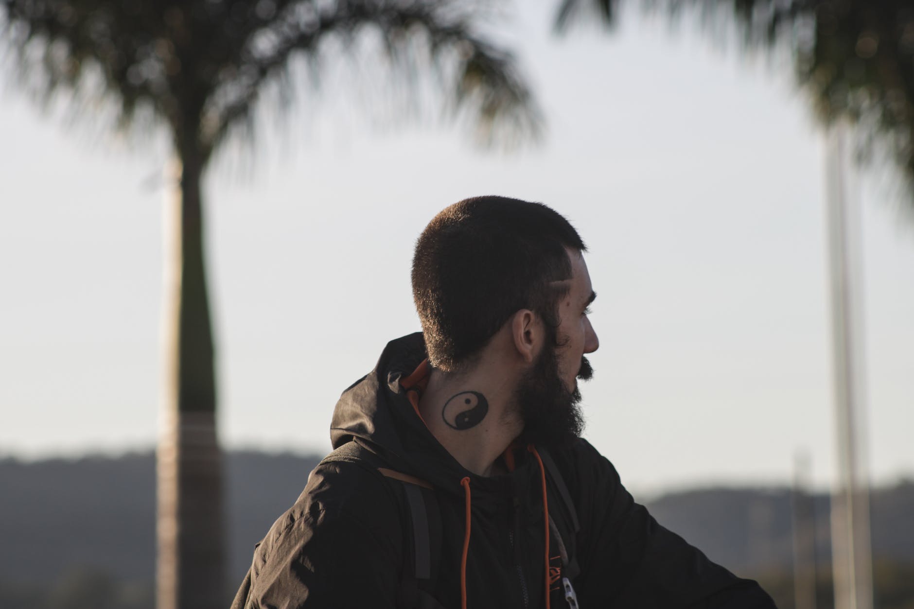 a tattooed man wearing hoodie jacket while looking afar