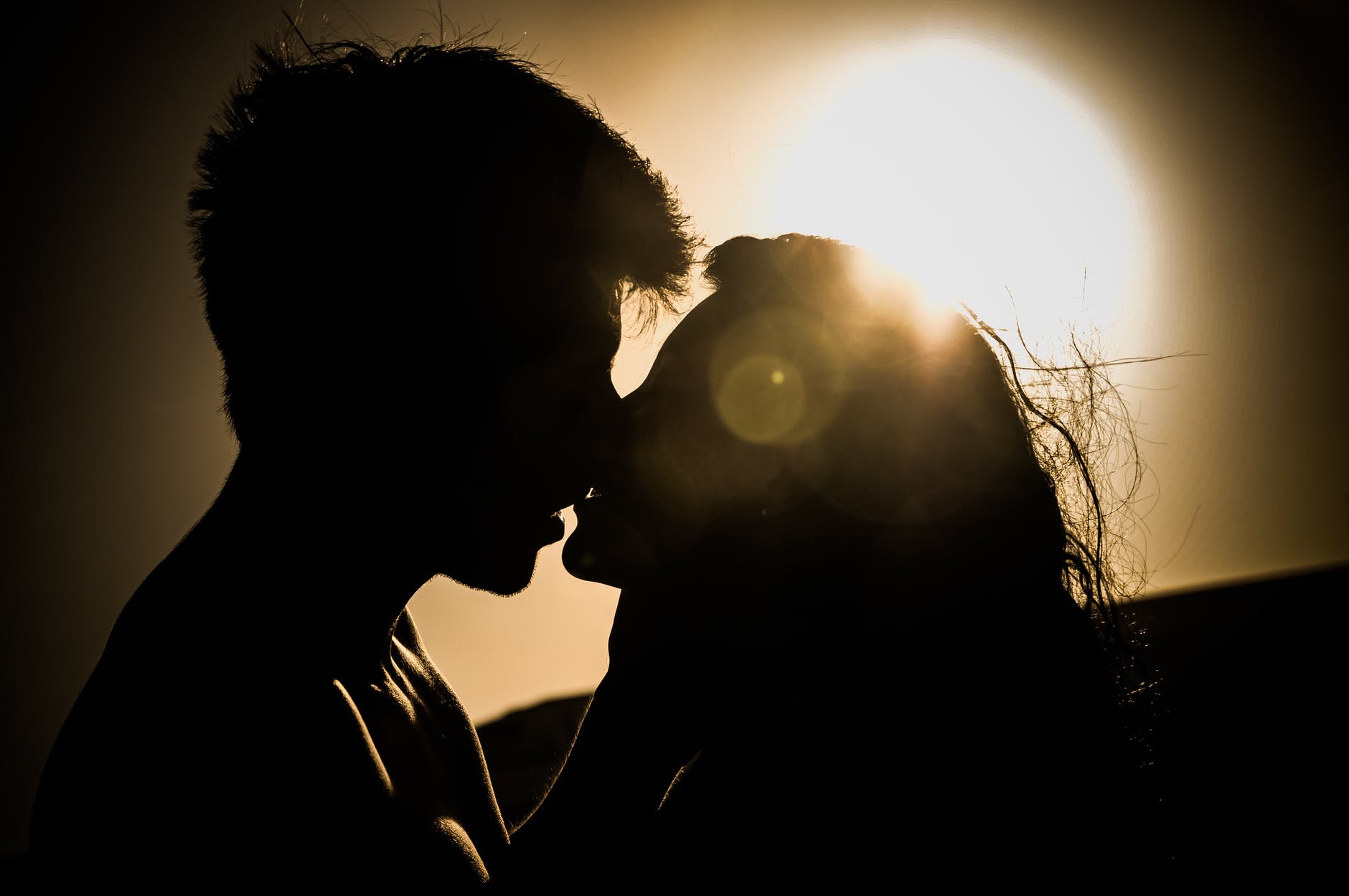 silhouettes of couple kissing against sunset