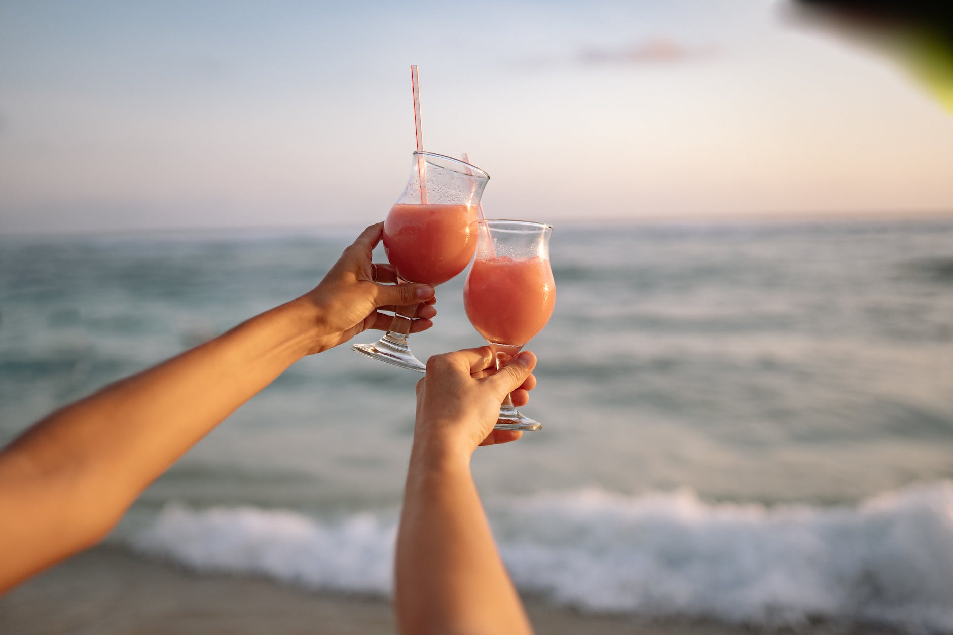 person holding clear wine glass with pink liquid